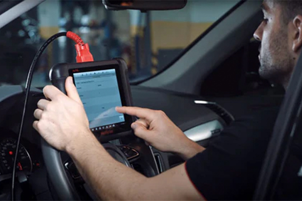 Tecnico Ambiorix sentado dentro del vehiculo realizando diagnostico con tester OBD avanzado